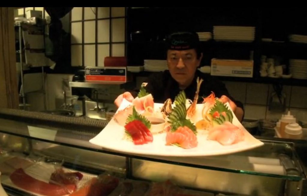 Sushi chef offering a plate of sushi over the bar at Osaka Japanese Bistro Las Vegas