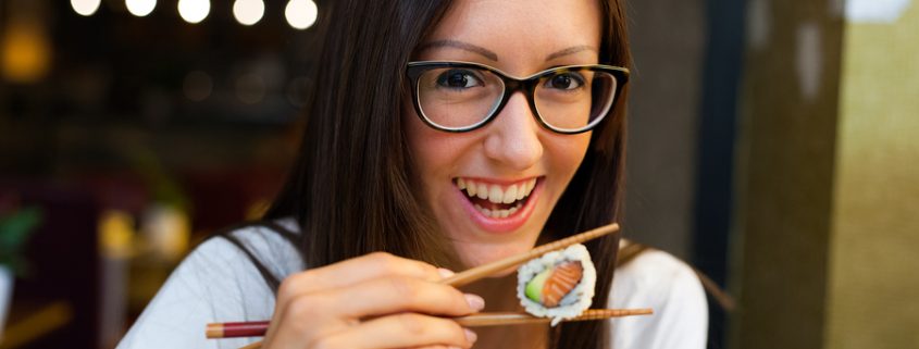 Smiling woman eating sushi with chopsticks in Japanese restaurant