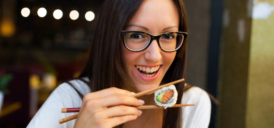 Smiling woman eating sushi with chopsticks in Japanese restaurant