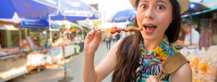 young girl traveler enjoying delicious grilled yakitori chicken skewers on street market in Japan