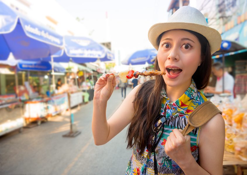 young girl traveler enjoying delicious grilled yakitori chicken skewers on street market in Japan