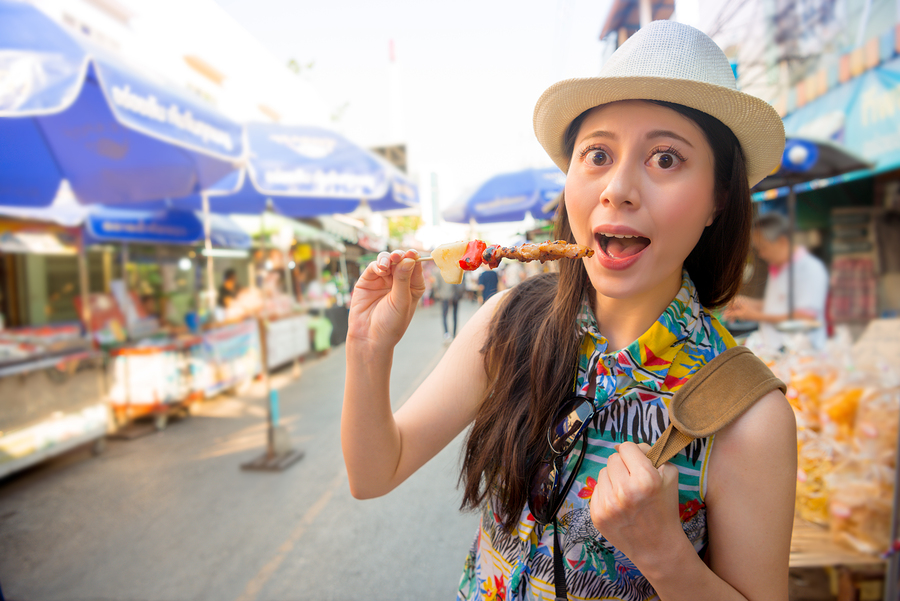 young girl traveler enjoying delicious grilled yakitori chicken skewers on street market in Japan